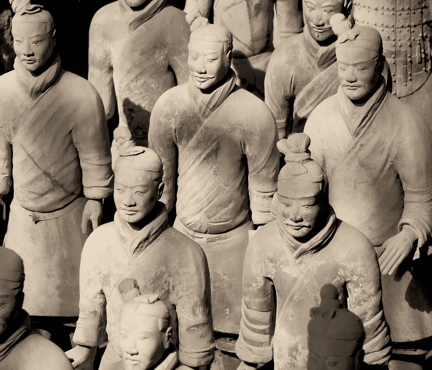 A sepia-toned, tightly framed photograph showcasing a dense cluster of life-sized Terracotta Warrior statues from China’s Qin Dynasty, each with individually sculpted facial features, distinct hairstyles, and detailed armor or robes, captured under dramatic lighting that emphasizes texture, weathering, and the solemn expressions of the ancient clay soldiers.